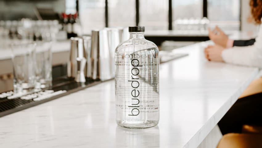 A bottle of bluedrop water from the bar150 product sitting on a bar table.