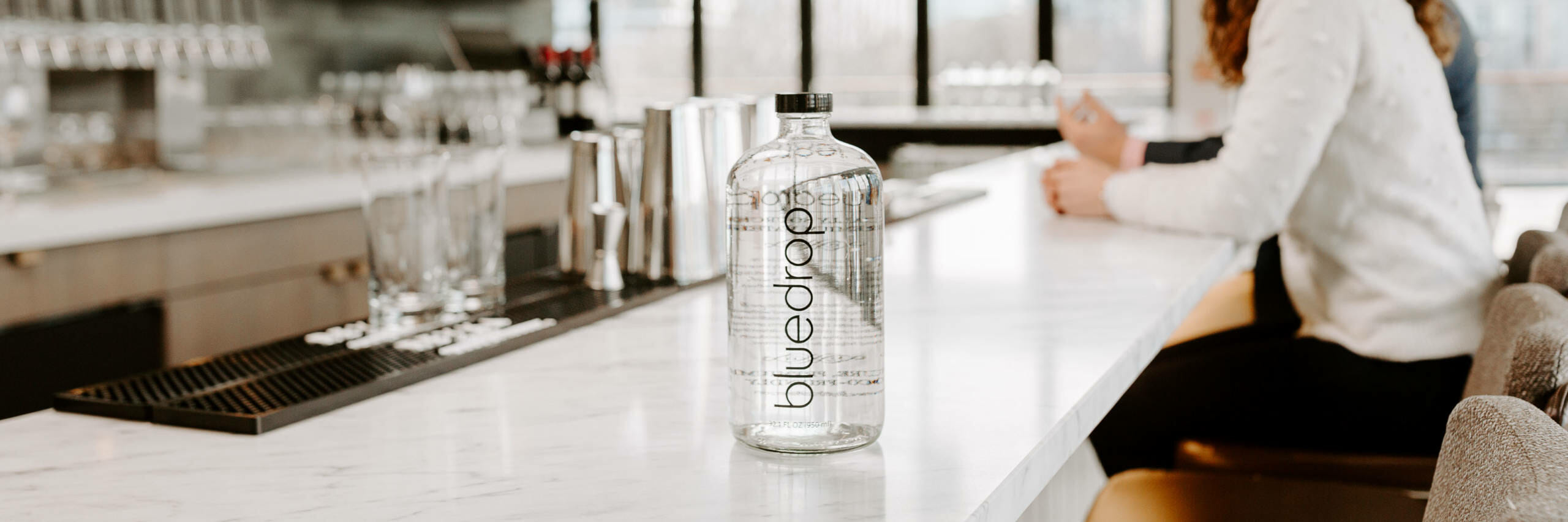 A bottle of bluedrop water from the bar150 product sitting on a bar table.