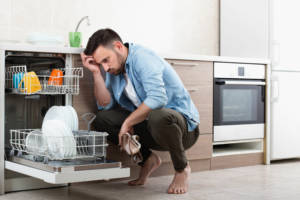 A man who is sad that his dishes are still dirty after running the dishwasher.