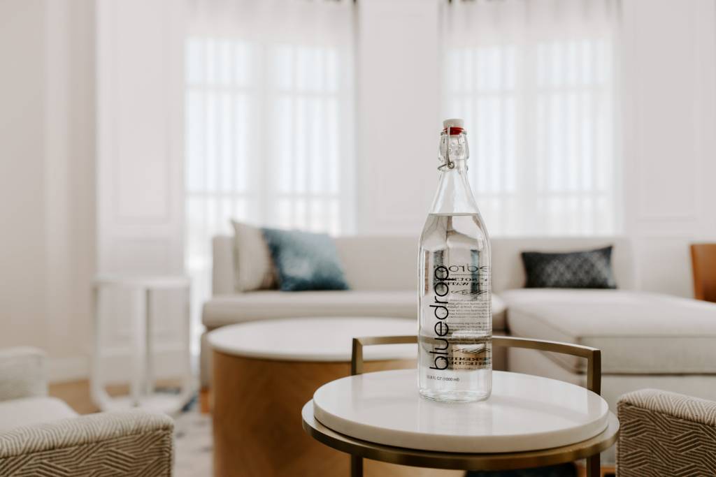 A tall glass bottle sits on a hotel room end table