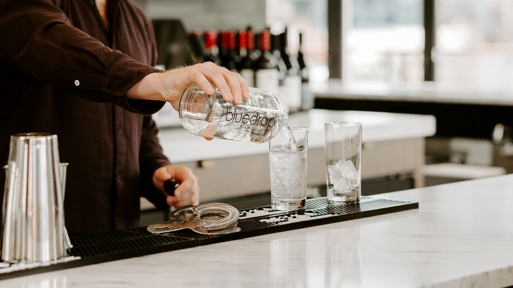 A bartender pouring water from a custom bluedrop branded bottle.