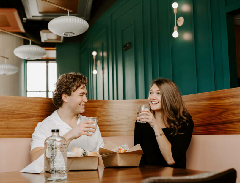 Two people enjoying their food at a restaurant with a glass of bluedrop water on the table.