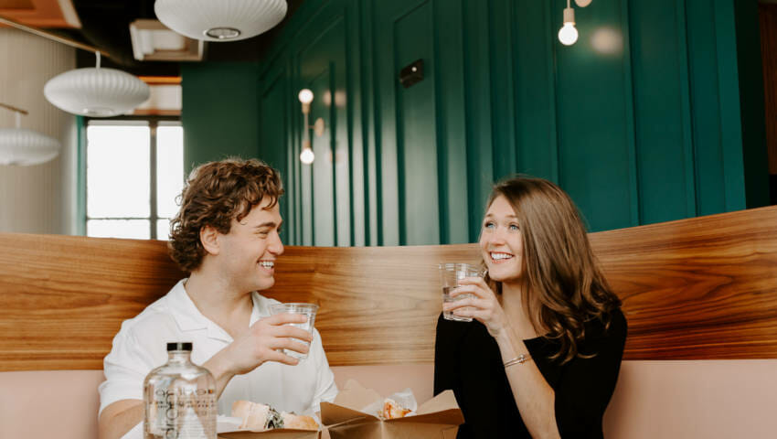 Two people enjoying their food at a restaurant with a glass of bluedrop water on the table.