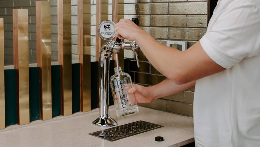 A person using a bluedrop water tower to fill their reusable glass bottle.