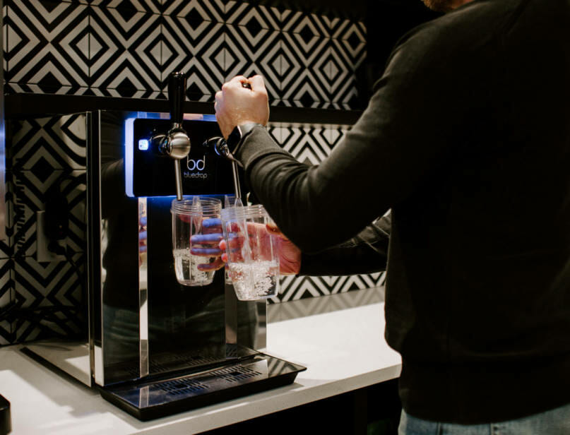 A person using the bluedrop water system to fill a glass of water.