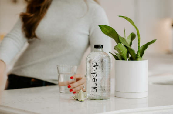 A person sitting at a counter with a glass of water and a bottle of bluedrop water on the table.