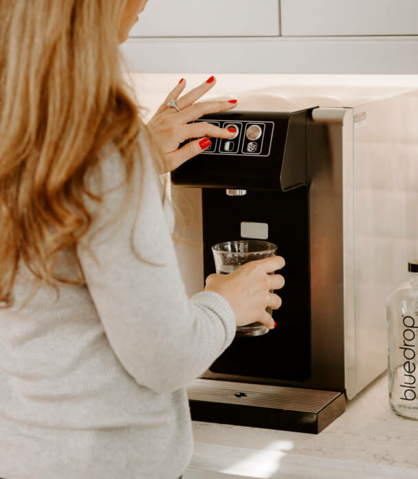 A person using their home still and sparkling system to fill a glass with water.