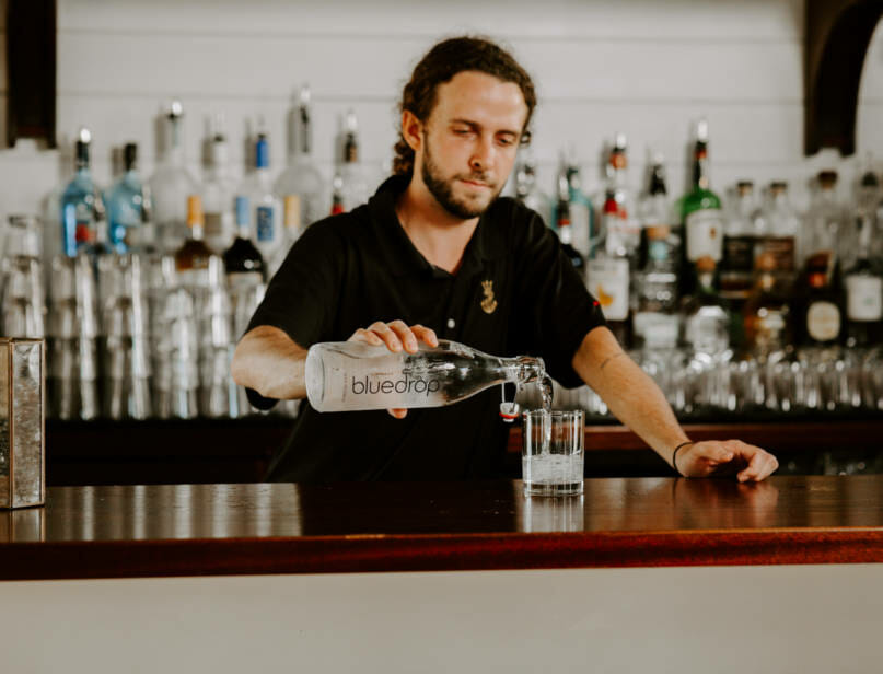 A person pouring water into a glass from a bluedrop water bottle at a bar.